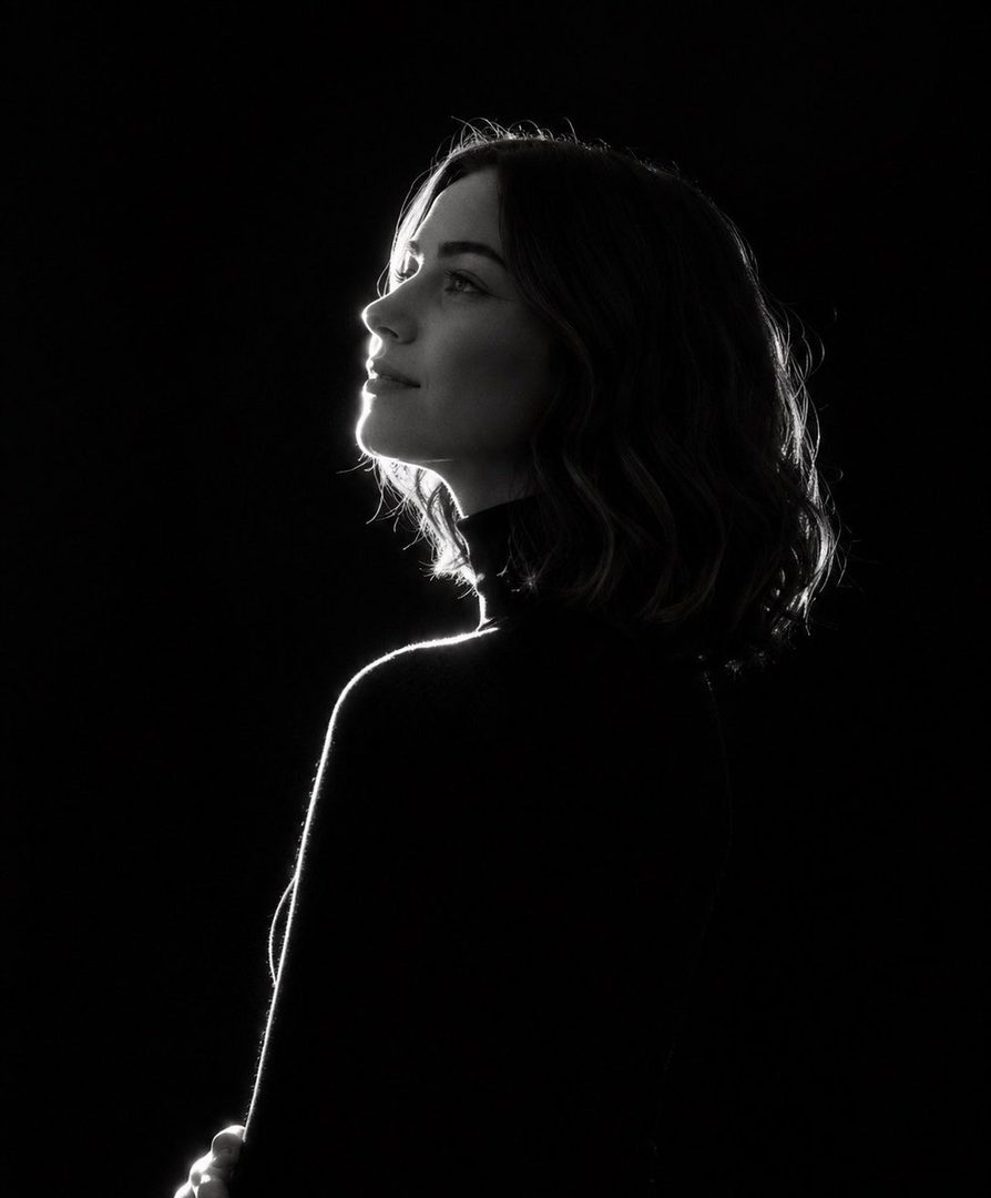 A black and white studio portrait of a woman with short dark hair, looking up and to the side, with dramatic rim lighting against a black background.