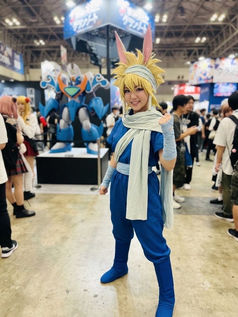 A young woman in a blue costume with rabbit ears and a light scarf poses at an indoor event.