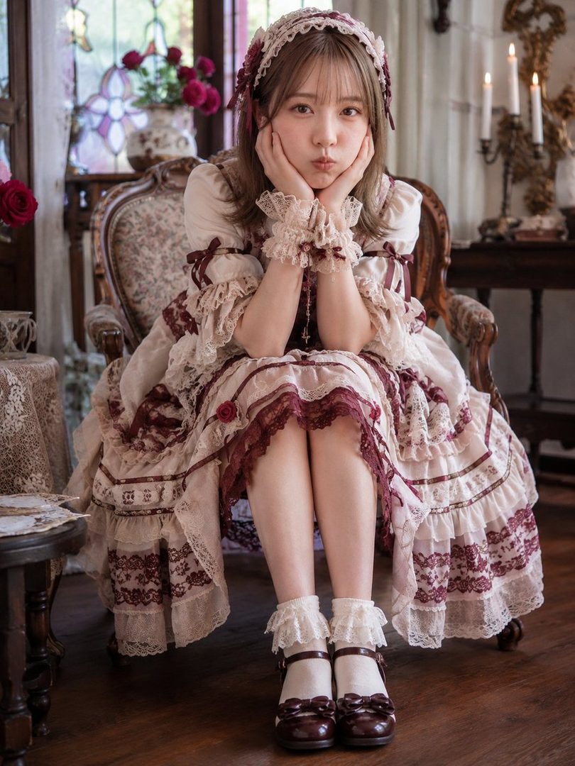 A young woman in a gothic lolita dress sits in an antique chair, posing with her hands on her cheeks.
