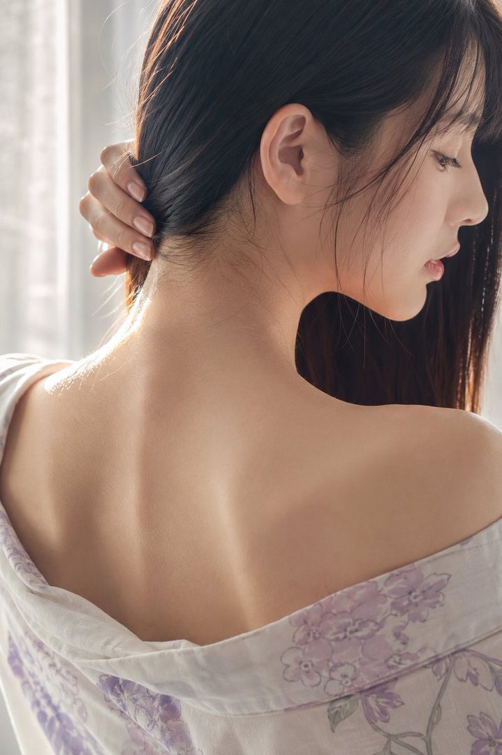 Close-up profile of a young woman's neck and shoulder, with her hand touching her hair, soft natural light.