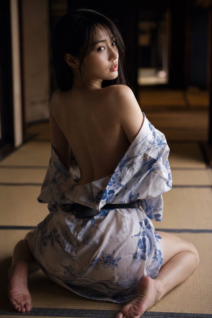 A Japanese woman in a blue and white yukata, posing indoors with her back to the camera.
