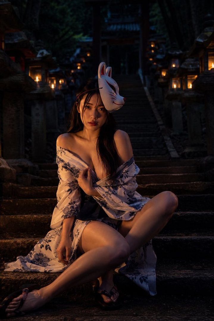 A woman in a yukata and a fox mask sits on stone steps at night, with lanterns illuminating the scene.