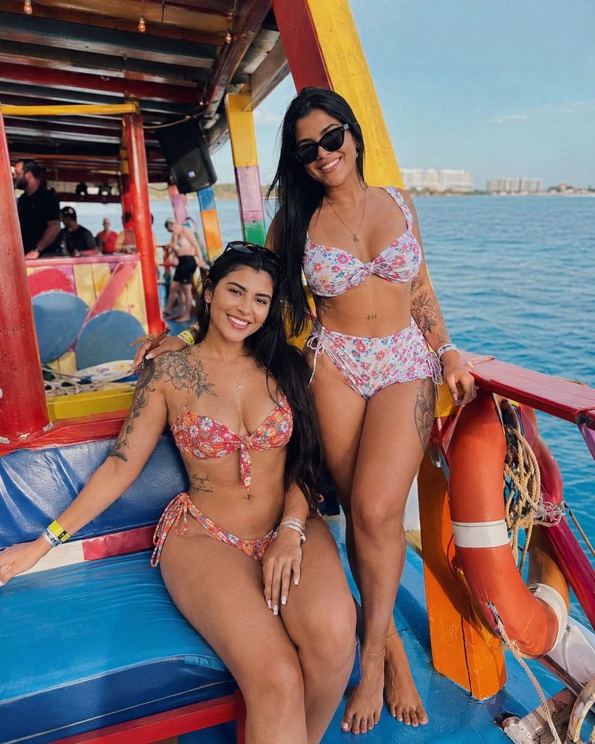 Two young women in floral bikinis posing on a boat in the Caribbean Sea.