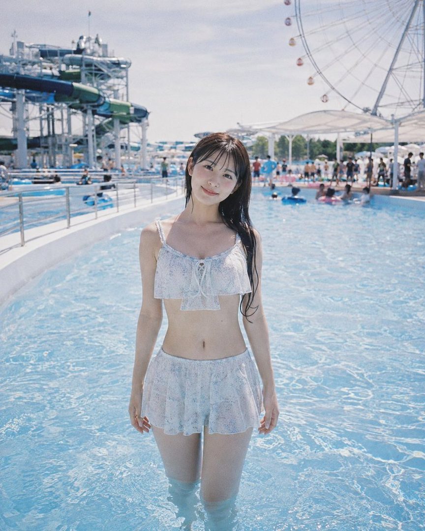 A young woman in a floral bikini stands in a swimming pool at a water park, smiling at the camera.