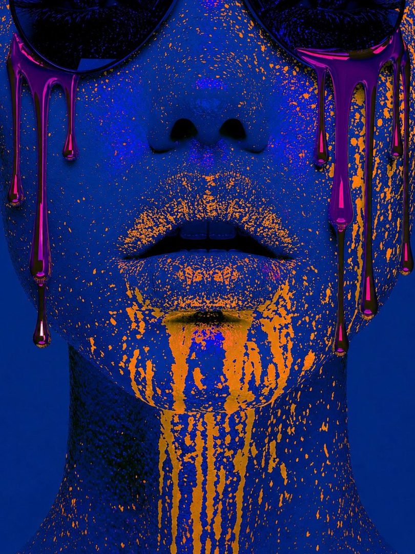 Close-up portrait of a person with blue skin covered in orange paint splatters and purple drips, wearing sunglasses.