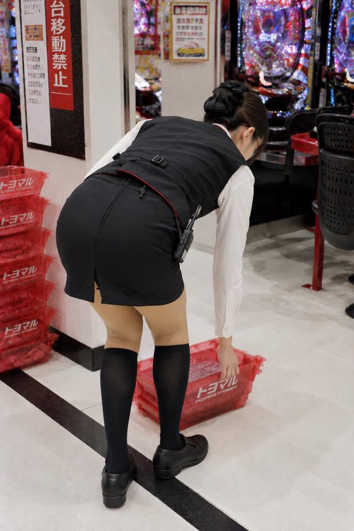 A woman in a black vest and white shirt bends over, showing her back and legs in black stockings.