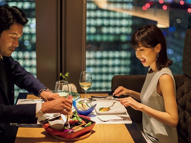 A man and a woman are enjoying a romantic dinner date at a restaurant with a city view at night.