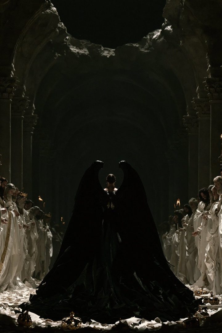 A figure with large black wings stands in a dark, ornate hall, surrounded by people in white robes holding torches.