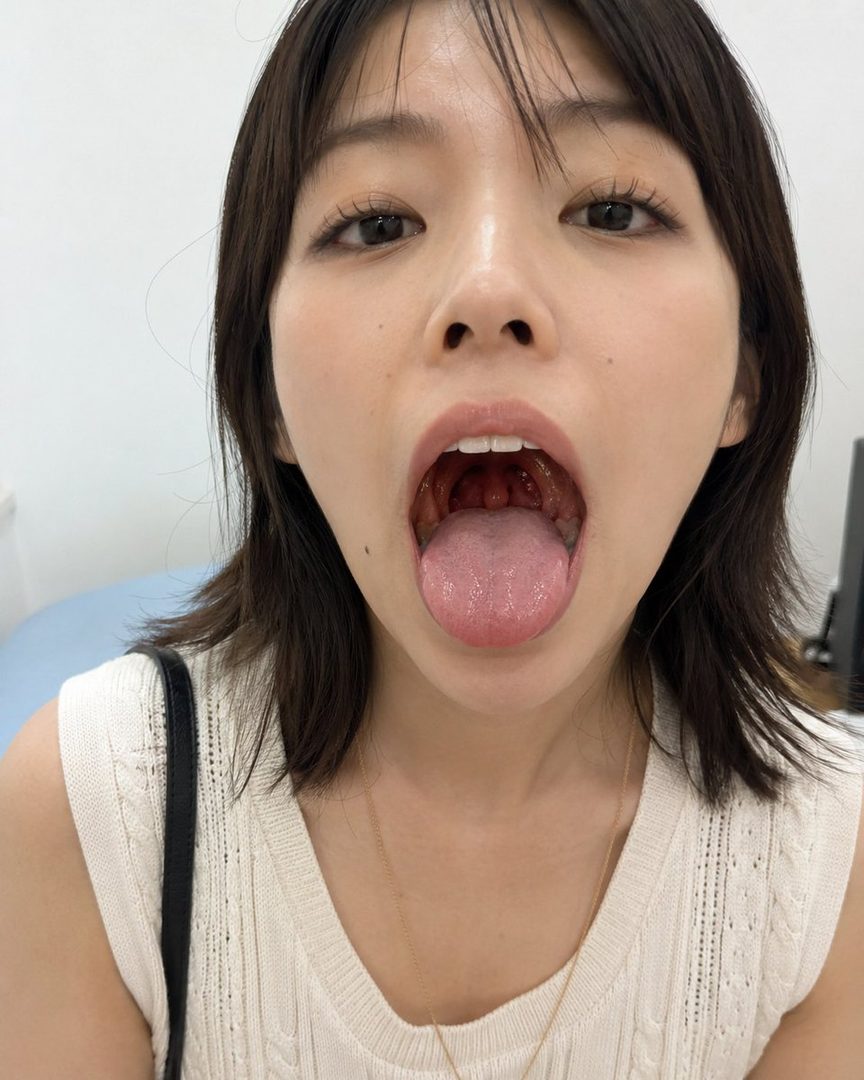 Close-up portrait of a young East Asian woman with her mouth wide open, showing her tongue and throat.