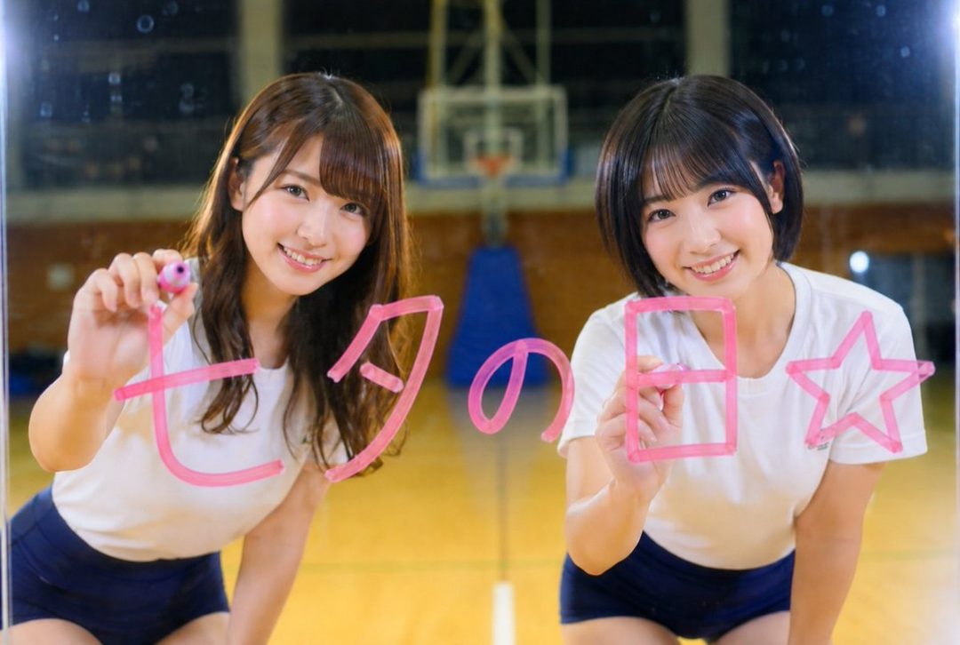 Two young women in athletic wear smile and draw characters on a glass surface in a gymnasium.
