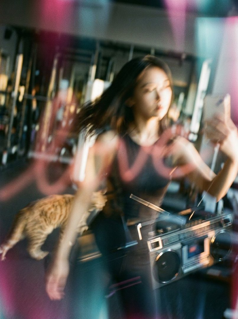 A young woman takes a selfie in a gym with a boombox and a cat.