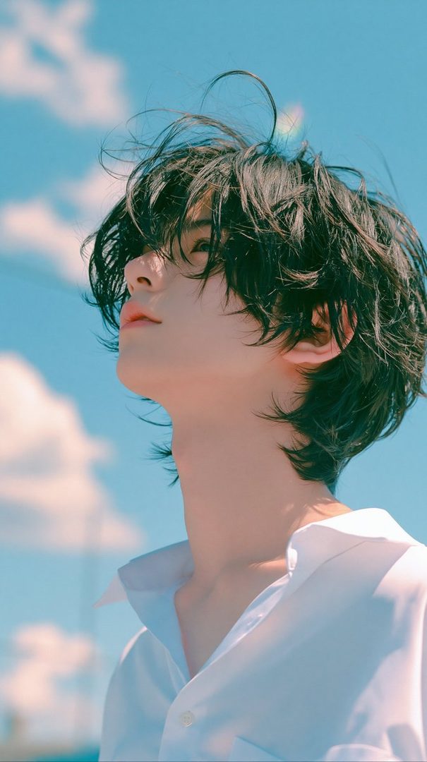 A young person with messy black hair looks up at the sky, wearing a white collared shirt.