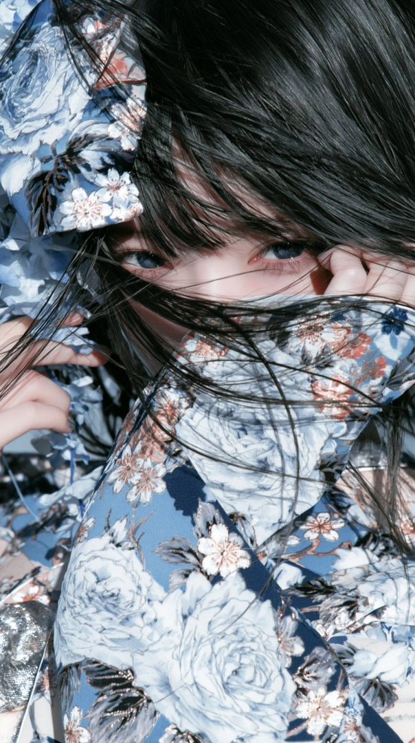 Close-up portrait of a young woman with black hair partially obscuring her face, wearing a floral print blouse.
