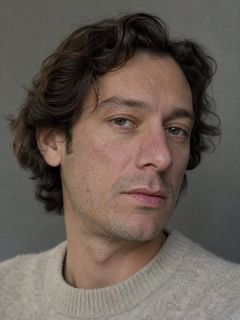 A realistic portrait of a man with wavy brown hair and a light-colored sweater, looking directly at the camera.