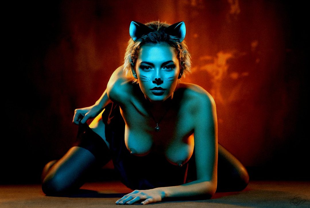A woman with cat ears and face paint poses suggestively in a studio setting.