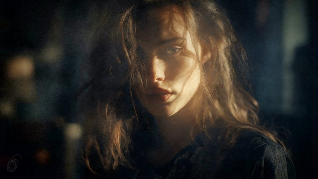 A close-up portrait of a young woman with long, wavy brown hair, her face partially obscured by shadows and light, looking directly at the camera with a serene expression.