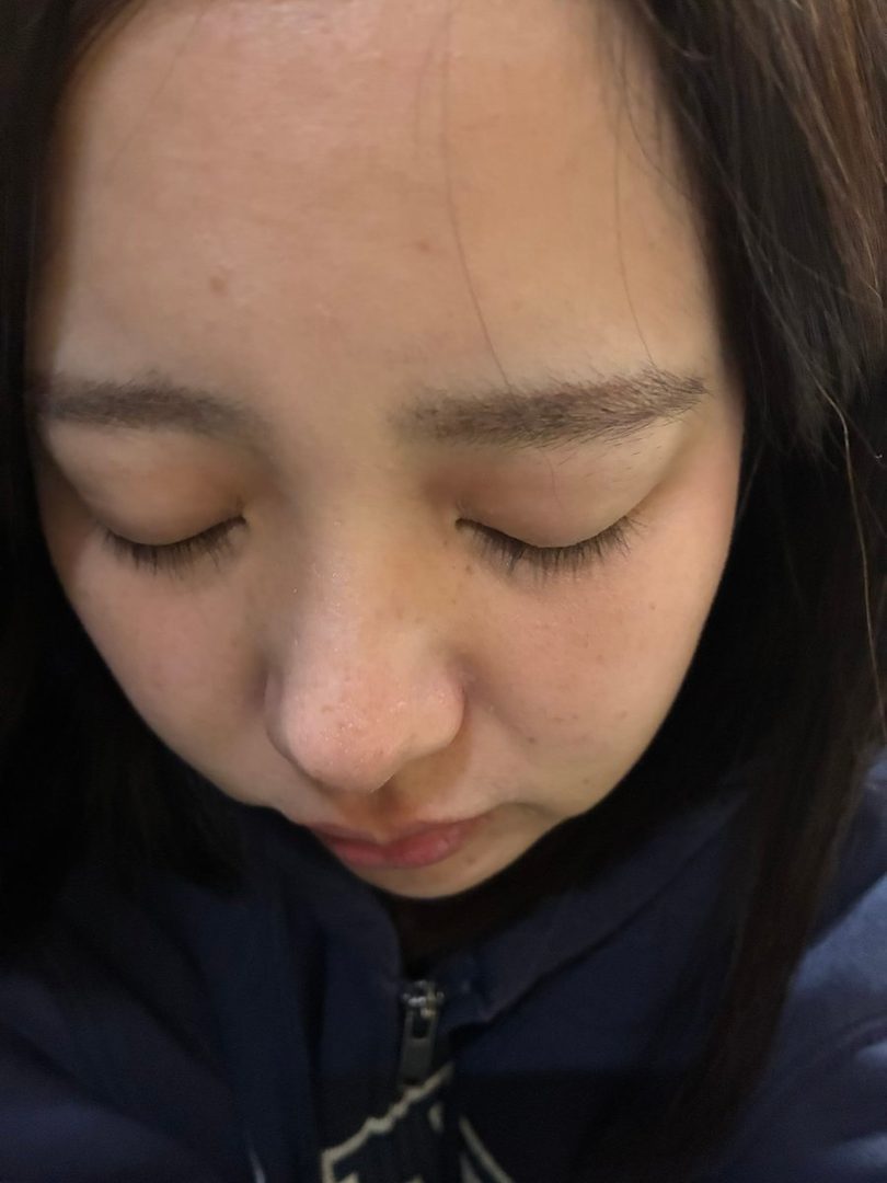 Close-up selfie of a young East Asian woman with her eyes closed, wearing a blue hoodie.