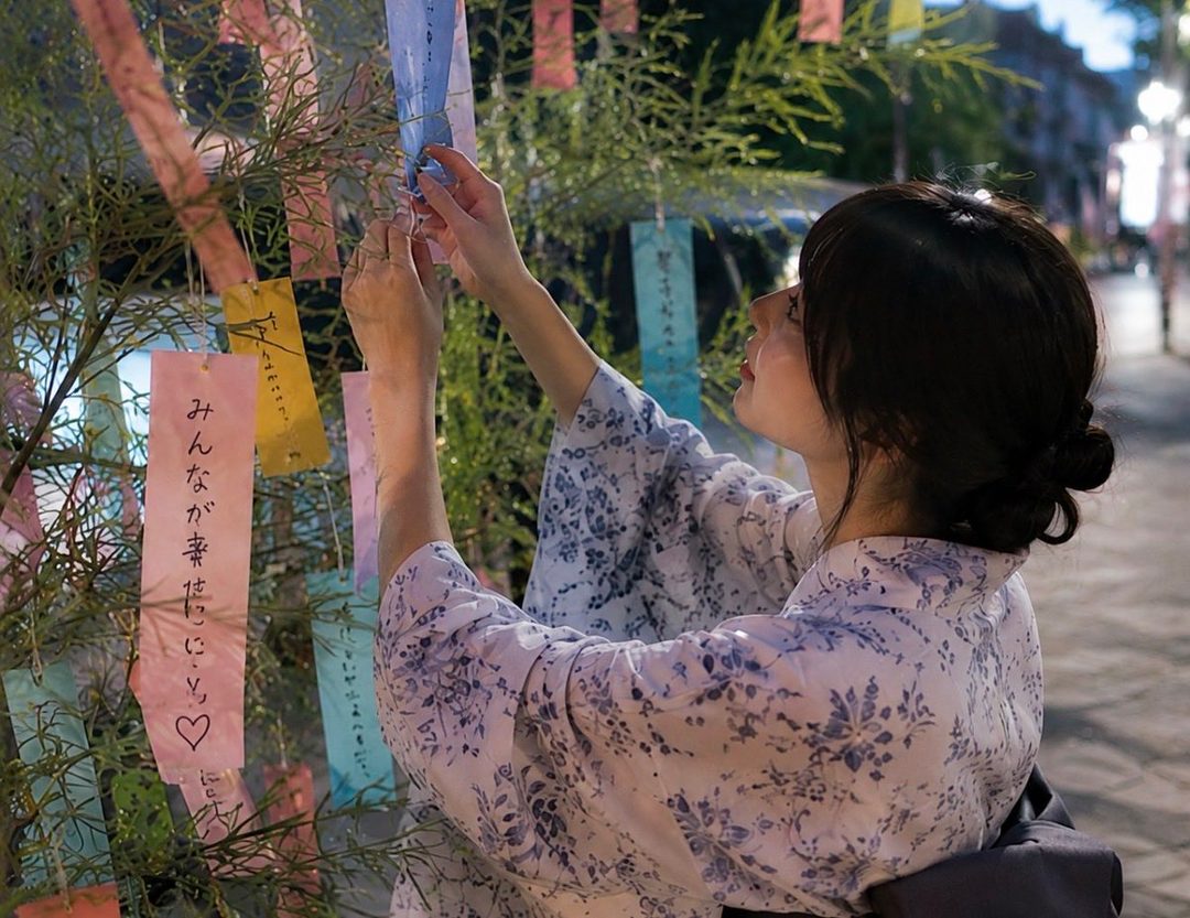 A young woman in a yukata ties a wish to a bamboo tree during the Tanabata festival.