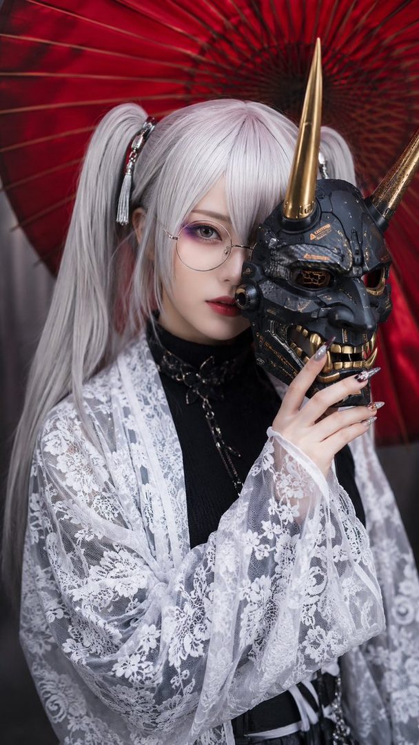 A woman with silver pigtails and glasses holds a black and gold oni mask, wearing a white lace kimono over a black top, with a red umbrella in the background.