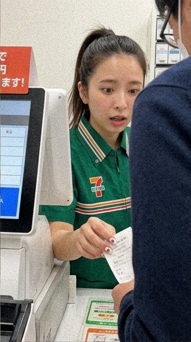 A young woman in a Seven-Eleven uniform handing a receipt to a customer.