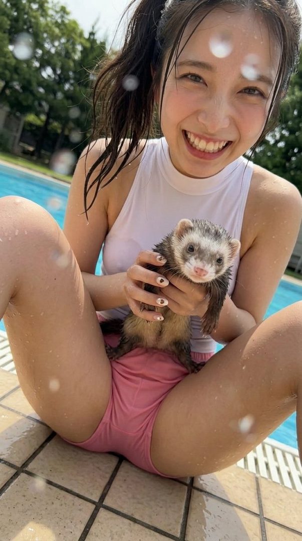 A smiling young woman in a white top and pink bottoms holds a ferret by a swimming pool.