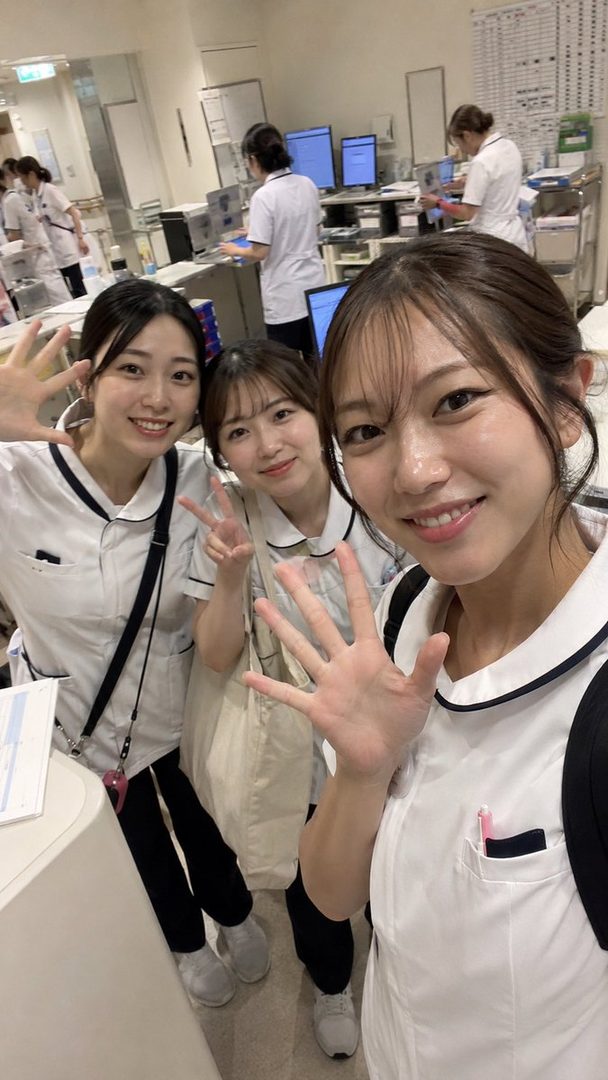 Three young women in nurse uniforms smiling and waving, possibly nursing students on a break in a hospital setting.