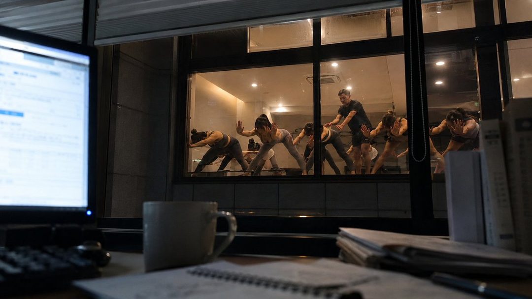 A group of people practicing yoga in a studio, viewed through a window at night.