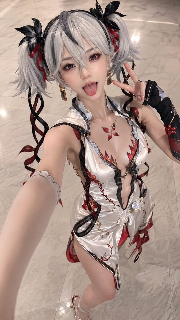 A young woman with silver twin-tail hair, wearing a white and red ornate dress, sticks out her tongue and makes a peace sign.