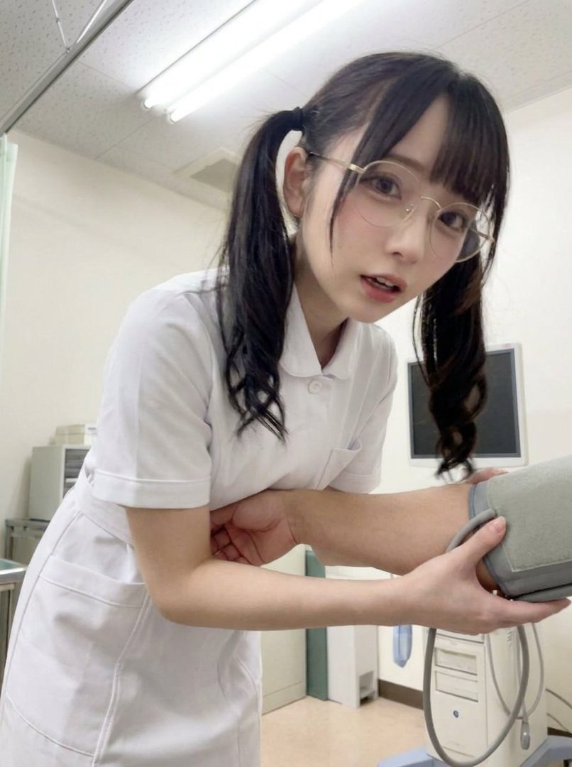 A young woman in a nurse's uniform and glasses with her hair in pigtails, taking a blood pressure reading.