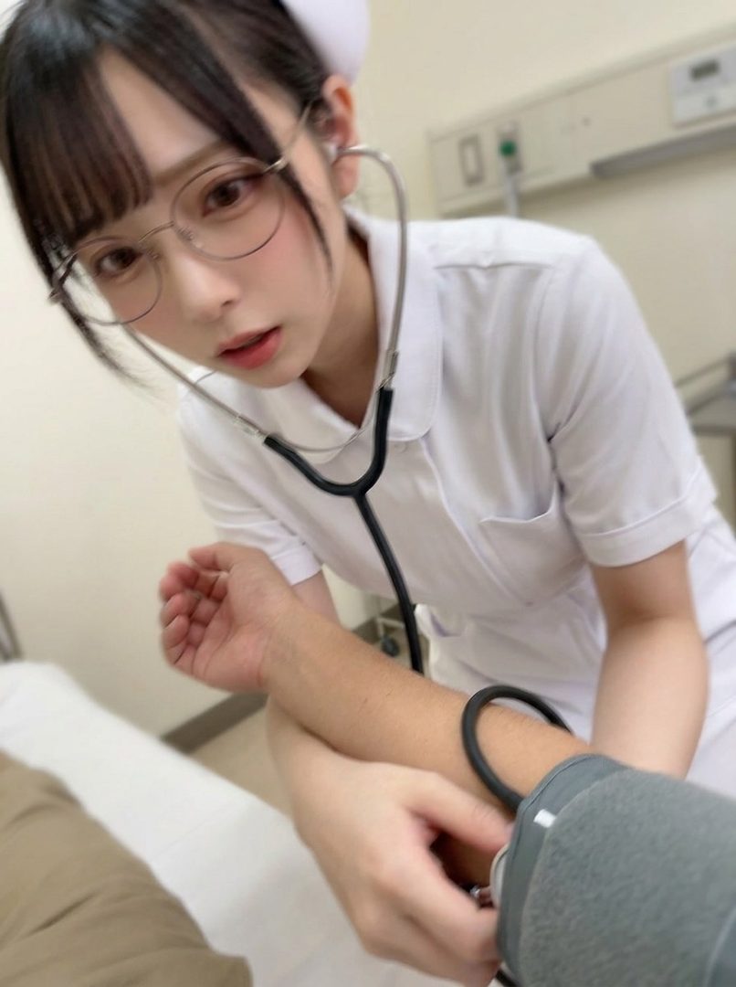 A young Japanese nurse wearing glasses and a nurse cap is taking a blood pressure reading with a stethoscope in a medical room.