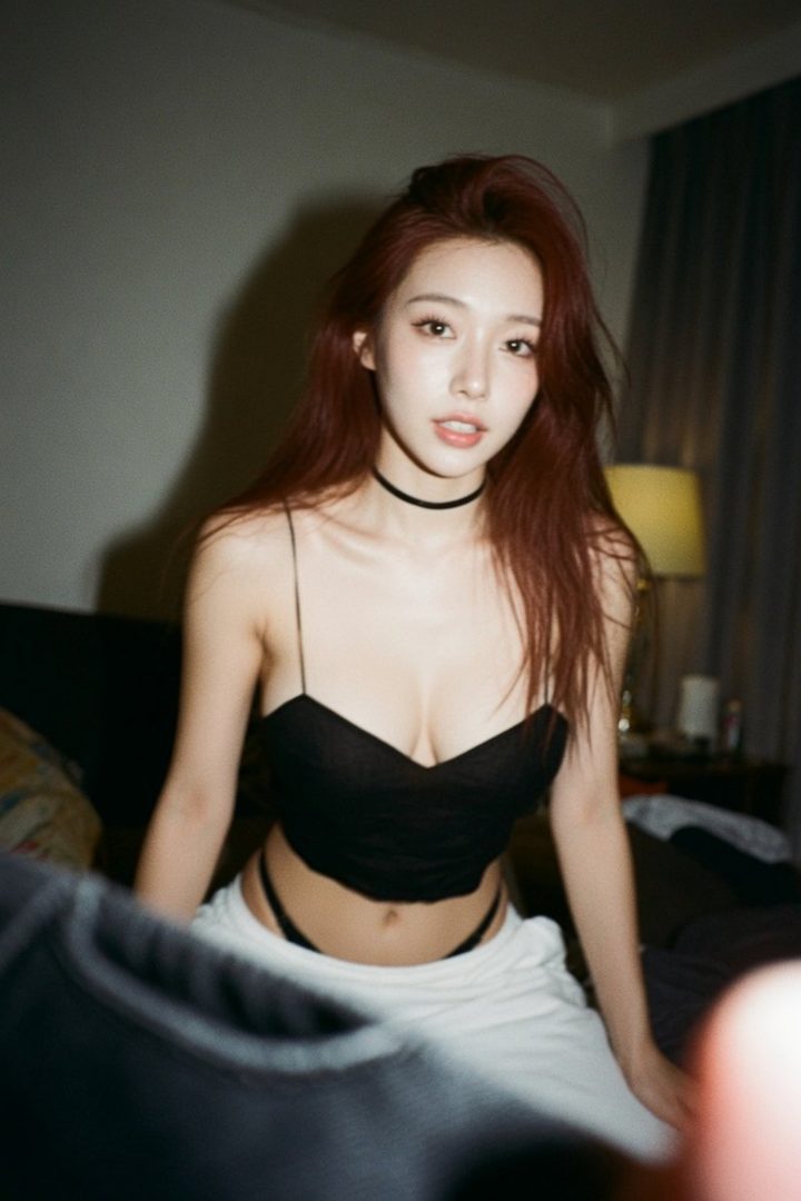 A young East Asian woman with long, reddish-brown hair and a black choker necklace, wearing a black crop top and white pants, posing indoors.