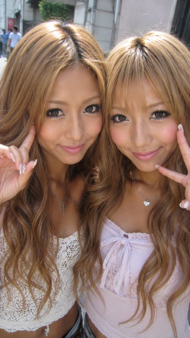 Two young women with long blonde hair posing for a selfie outdoors.