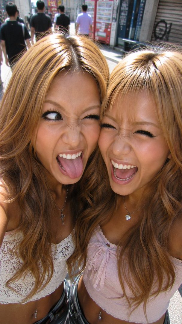 Two young women with blonde hair making funny faces at the camera on a sunny street.