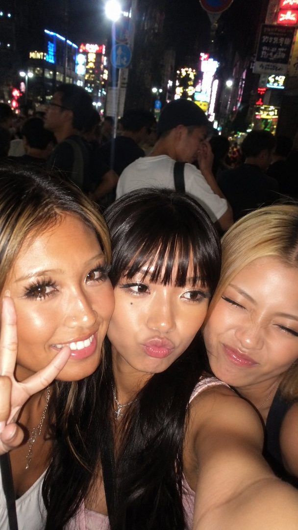 Three young women taking a selfie at night on a busy street with neon lights.