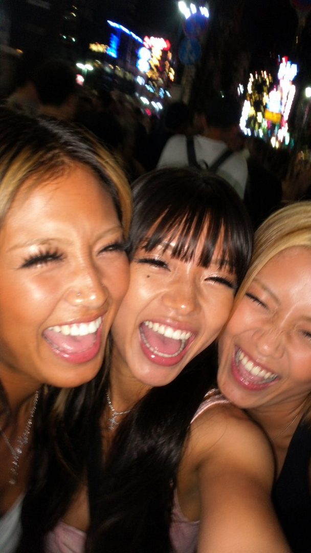 Three young women laughing together at night with city lights in the background.