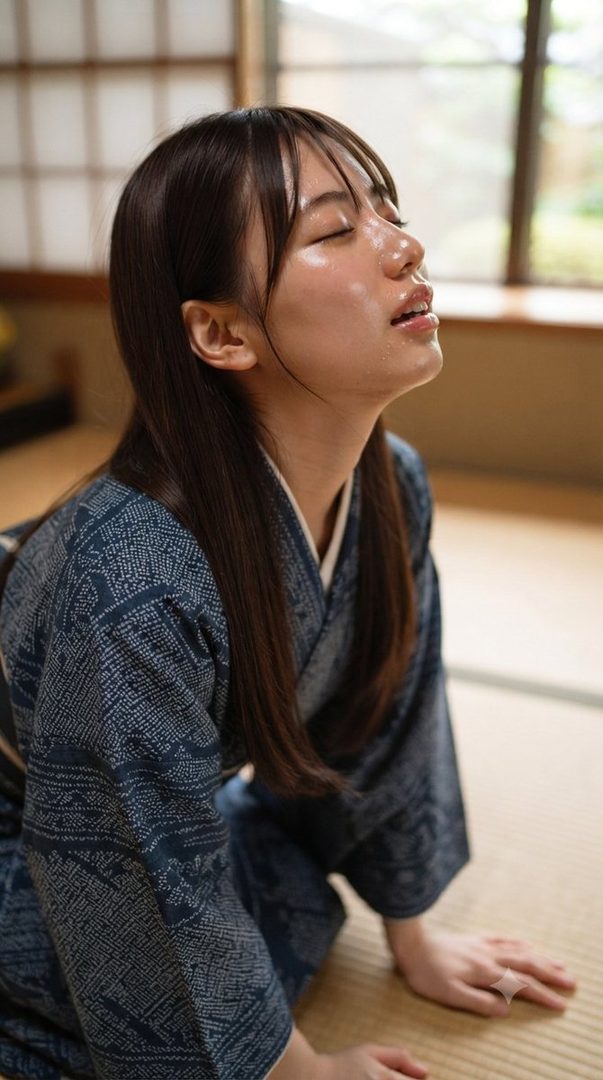 A young woman in a dark blue kimono with a white pattern sits on a tatami mat, her eyes closed and face tilted upwards, bathed in soft light.