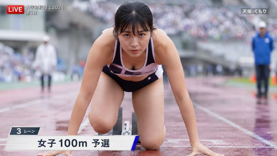 A female athlete in a black and white track uniform is in a starting block position on a wet track, looking intensely at the camera during a 100m race.