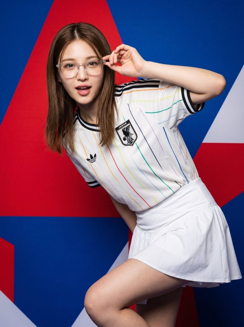 A young woman with long brown hair and glasses poses in a white Japan FIFA World Cup jersey with colorful stripes and a white mini skirt against a red, white, and blue geometric background.