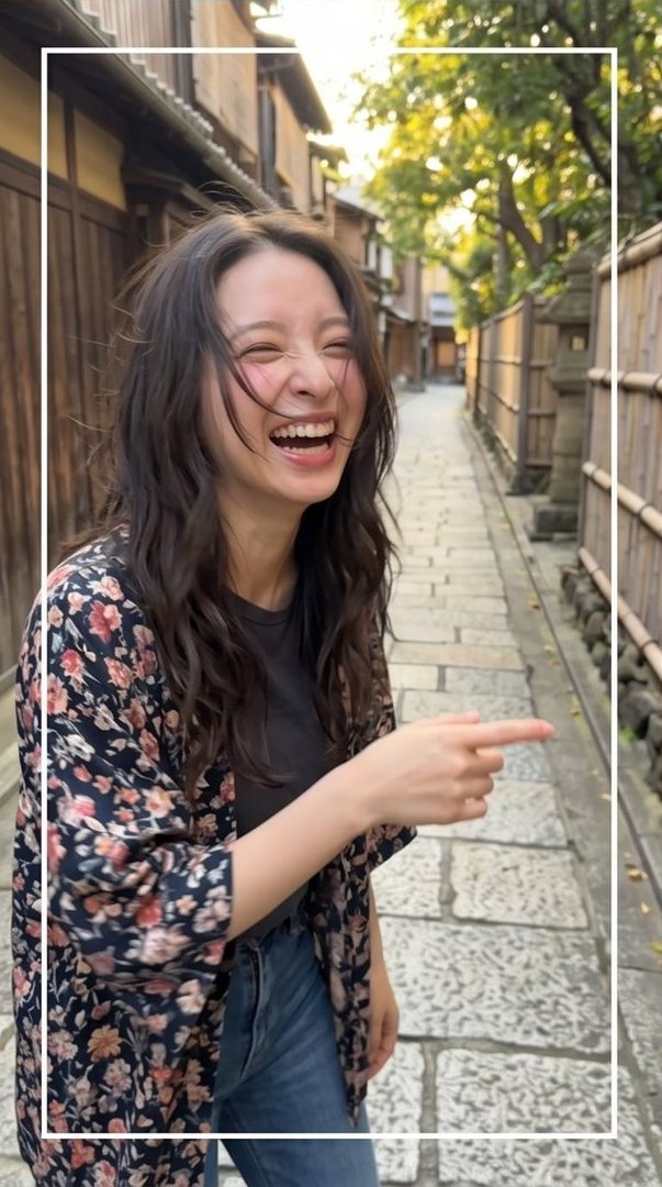 A young woman with long, dark, wavy hair laughs heartily while pointing to the side on a narrow street lined with traditional Japanese buildings.