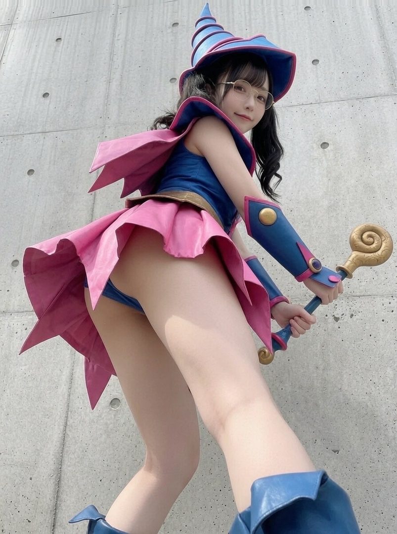 A young woman in a Dark Magician Girl cosplay, wearing a blue and pink outfit with a pointed hat and holding a staff, posing outdoors.