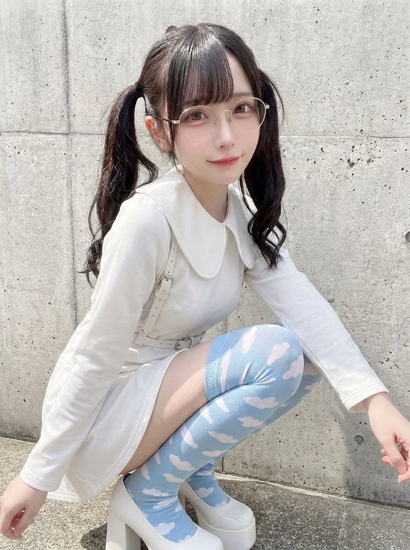 A young woman with black twin-tail hair and glasses, wearing a white outfit and blue cloud-patterned thigh-high socks, squats outdoors.