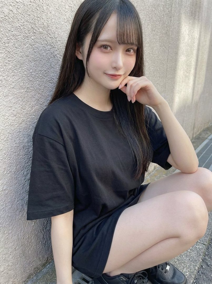 Young East Asian woman with long straight black hair and bangs wearing an oversized black t-shirt, posing outdoors against a textured wall.