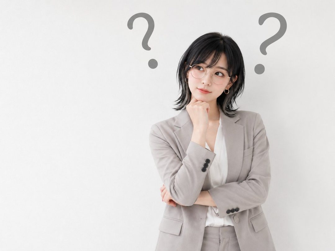 Young East Asian woman with short black hair and glasses wearing a light gray suit, posing thoughtfully with her hand on her chin against a white studio background with floating question marks.