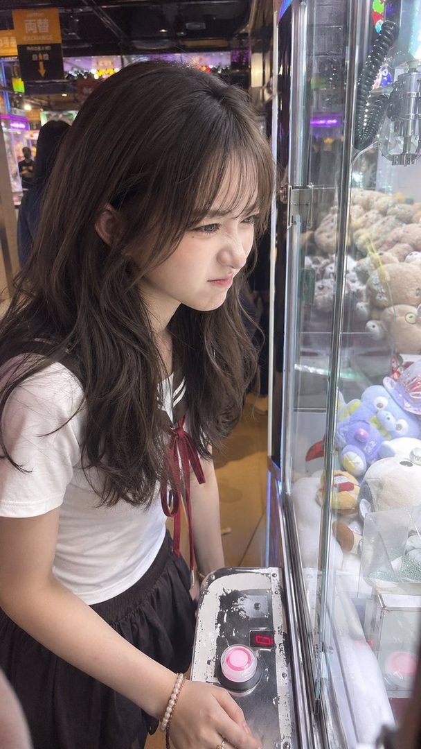 Young woman with long brown hair focused on operating a claw machine in a colorful arcade setting.
