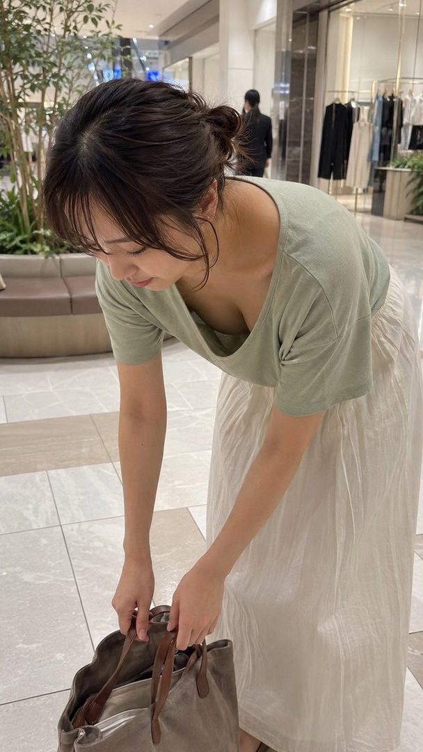 Young woman in a light green top and white skirt bending down to lift a bag inside a shopping mall.