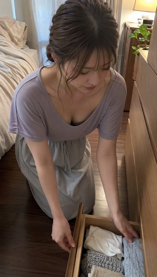 A young East Asian woman in a casual dress kneels beside an open wooden drawer in a sunlit bedroom, looking down at folded clothes.