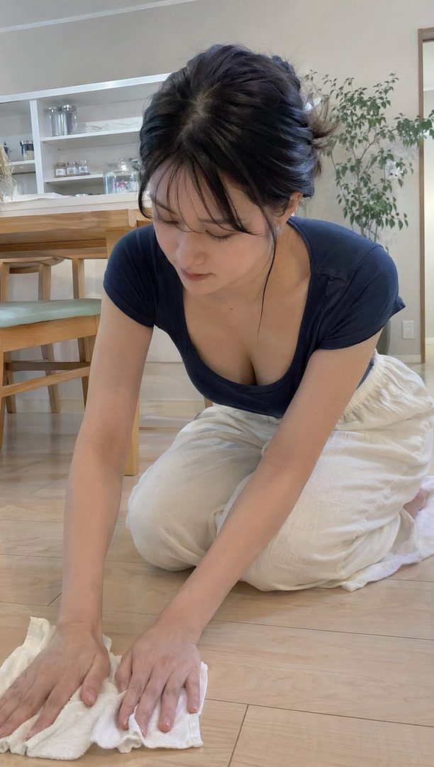 A young East Asian woman with dark hair in a casual top kneeling to wipe a wooden floor in a bright modern home interior.
