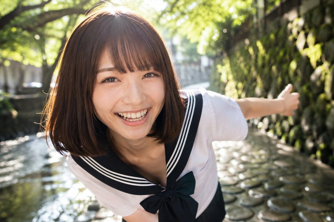 Smiling young Japanese woman in sailor school uniform posing happily outdoors by a sunlit canal.