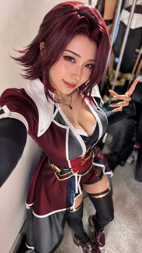 Woman with short red hair in a detailed maroon fantasy cosplay outfit taking a selfie indoors.