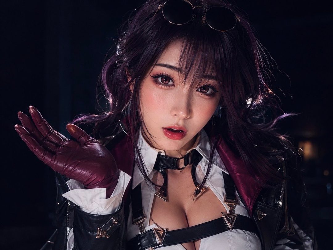Stylish young woman with long dark purple hair wearing a white blouse, black harness, and leather jacket in a dramatic studio portrait.